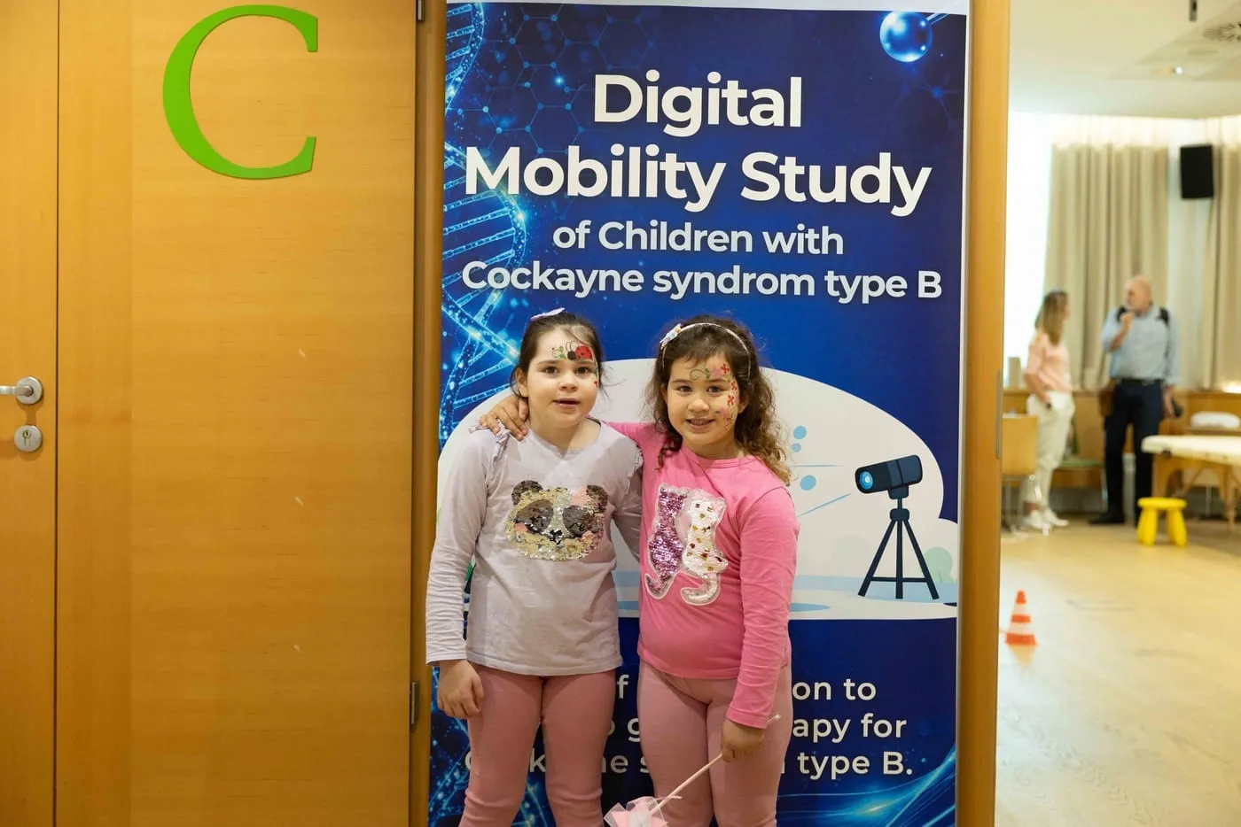 Two girls with Cockayne syndrome type B at the Digital Mobility Study banner during the conference in Ljubljana