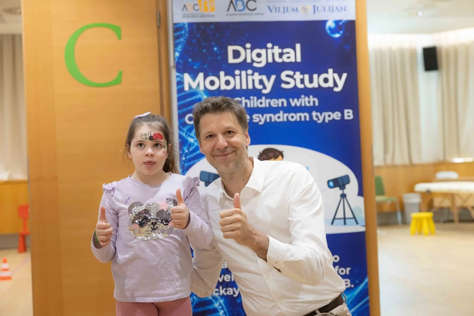 A girl with Cockayne syndrome type B with a researcher at the Digital Mobility Study banner during the Ljubljana conference